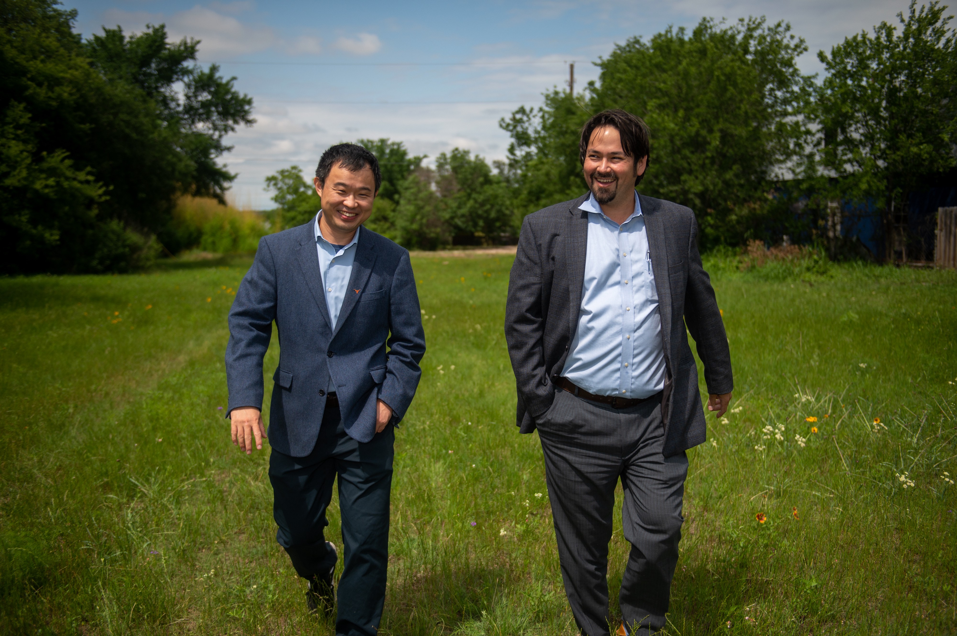 Two men, one a professor and another who works in transportation, walk through a grassy field where they plan to build a mobility hub.