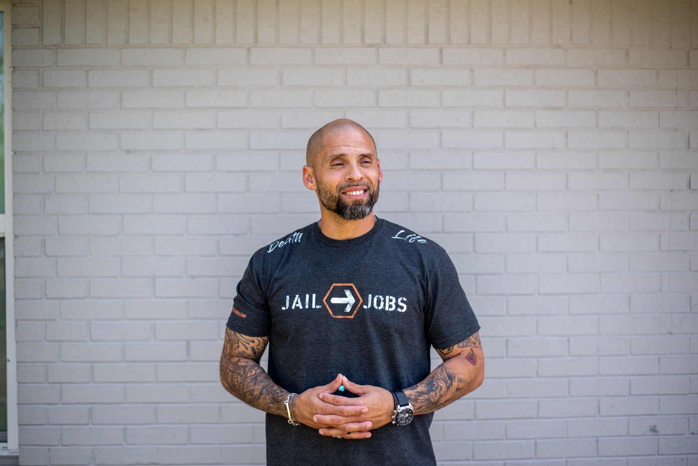 A nonprofit director who works to help previously incarcerated youth stands in front of a white brick wall.