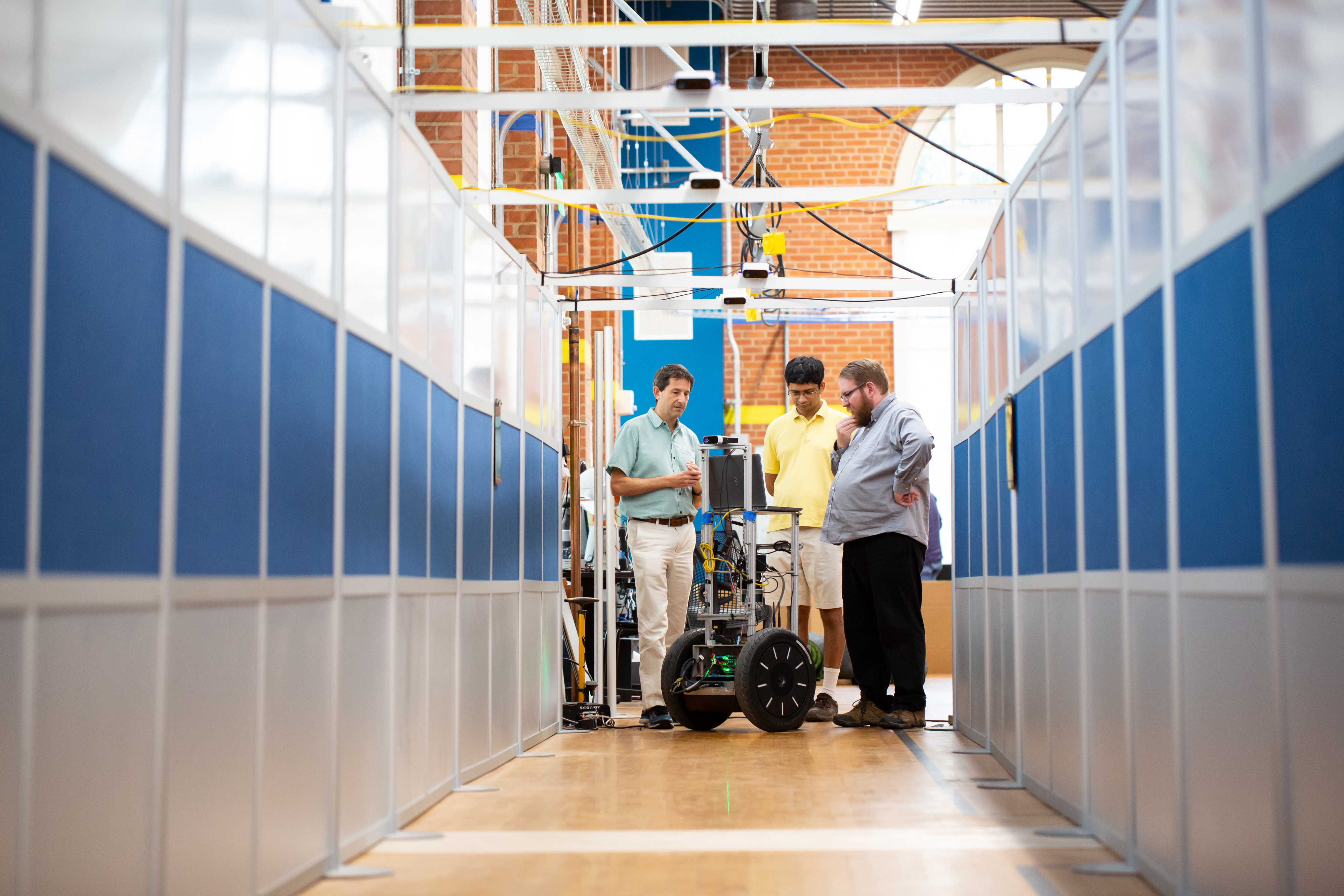 Three men stand around a robot on wheels in a robotic labs on the University of Texas at Austin campus.