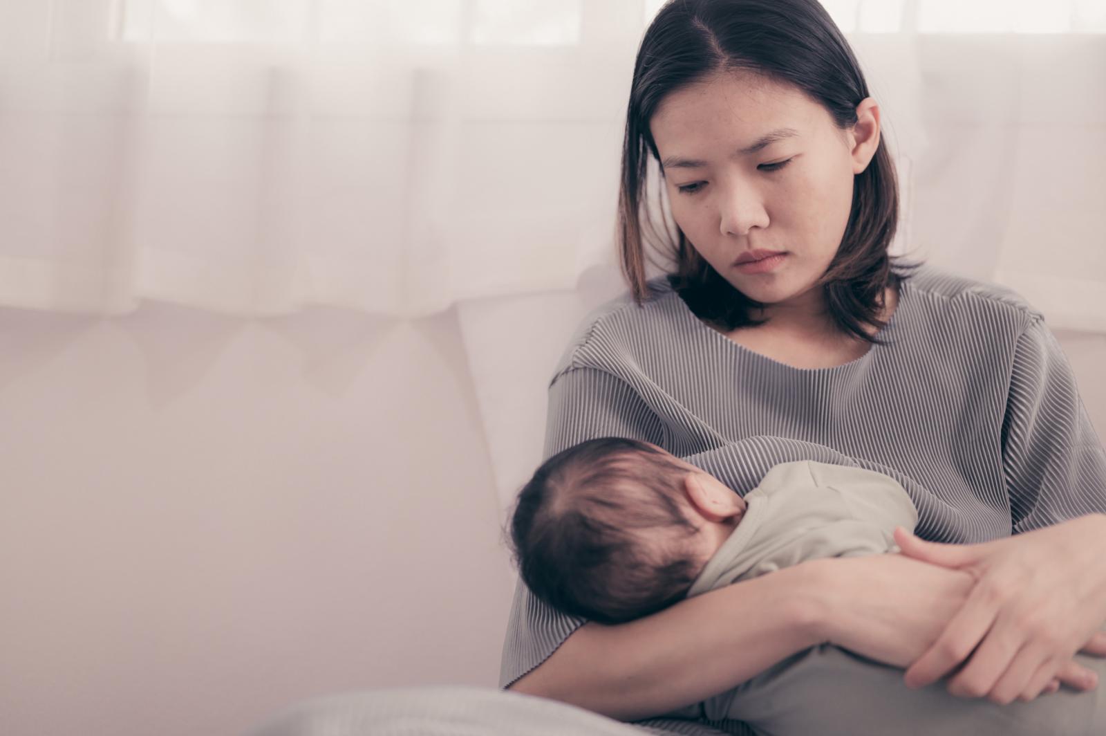A woman, looking sad, holds and nurses her baby.