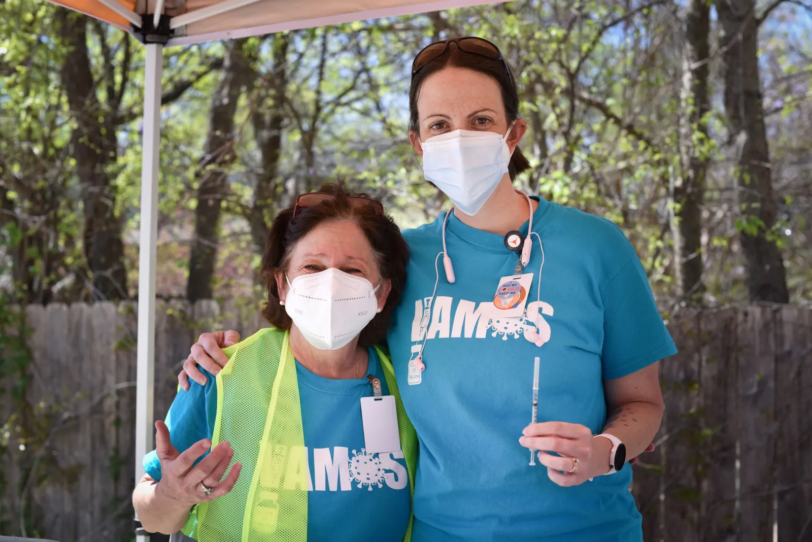 UT Nursing Associate Professor Karen Johnson is outside at a COVID-19 drive-through clinic in March 2021. She wears a face mask and holds a vaccine syringe and is standing next to a colleague also wearing a face mask.