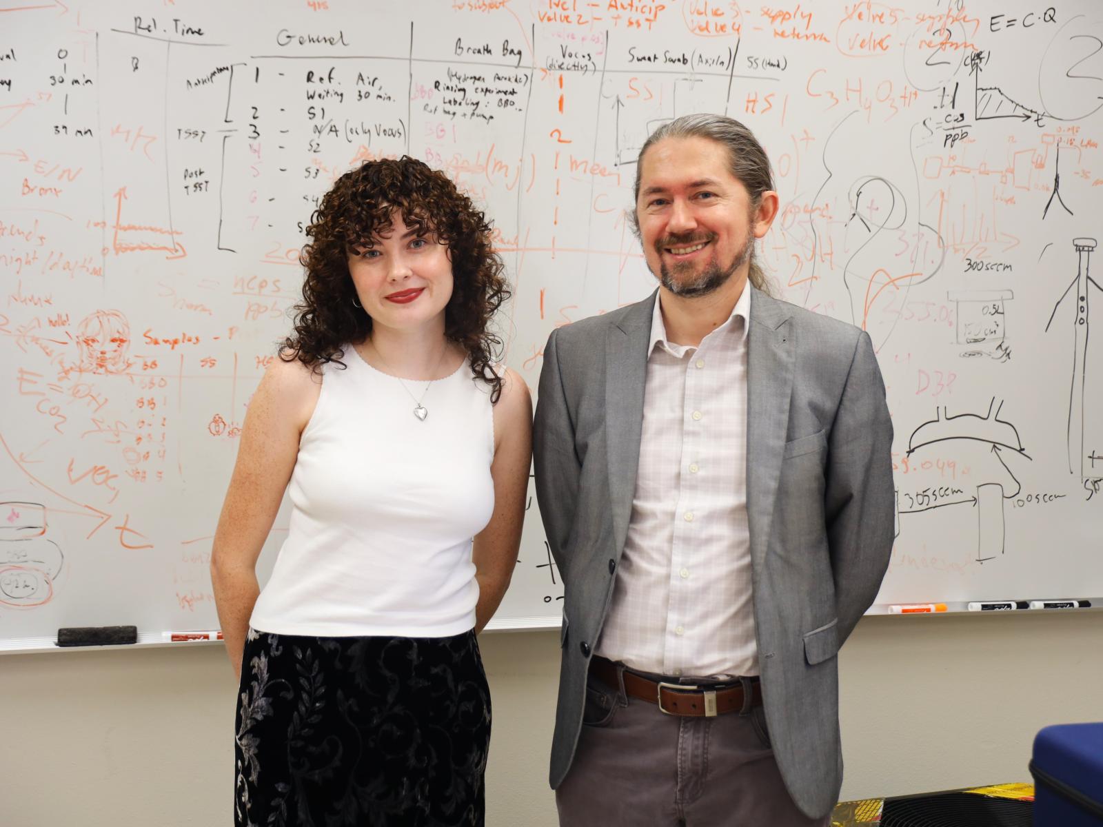 Ph.D. student Anna Neville and Professor Pawel Misztal stand in front of a whiteboard in Misztal's office. 