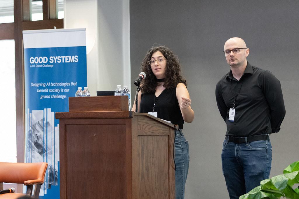 Project co-leaders Azza El-Masri, a graduate student, and Brad Limov, a postdoctoral researcher, present their findings at the 2025 Good Systems Symposium at UT Austin. El-Masri speaks behind a lectern; Limov stands next to her. Behind them is a Good Systems-branded roll-up banner. 