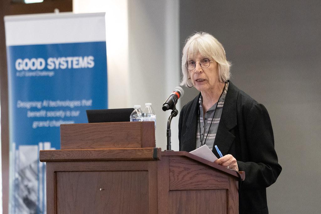 Sharon Strover, a professor in the Moody College of Communication and leader of Good Systems’ Being Watched research project, speaks at the 2025 Good Systems Symposium at UT Austin. Behind her is a Good Systems-branded roll-up banner. 