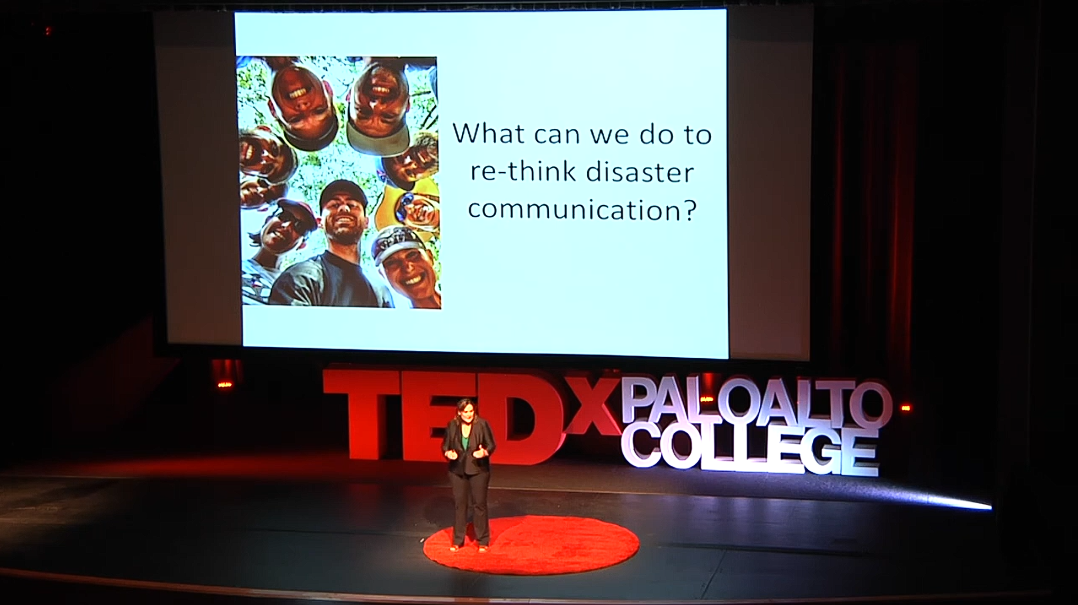 Keri Stephens speaks in a large auditorium at Palo Alto College. The slide behind her reads, "What can we do to re-think disaster communication?"