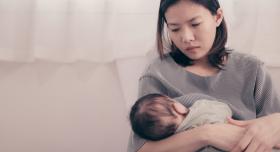 A woman, looking sad, holds and nurses her baby.