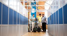 Three men stand around a robot on wheels in a robotic labs on the University of Texas at Austin campus.
