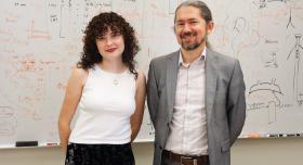 Ph.D. student Anna Neville and Professor Pawel Misztal stand in front of a whiteboard in Misztal's office. 