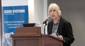 Sharon Strover, a professor in the Moody College of Communication and leader of Good Systems’ Being Watched research project, speaks at the 2025 Good Systems Symposium at UT Austin. Behind her is a Good Systems-branded roll-up banner. 