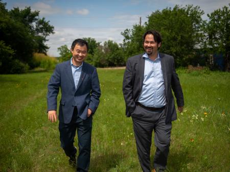 Two men, one a professor and another who works in transportation, walk through a grassy field where they plan to build a mobility hub.