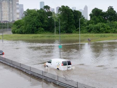 A van driving along a road in Houston, Texas is submerged in water during a flood event.