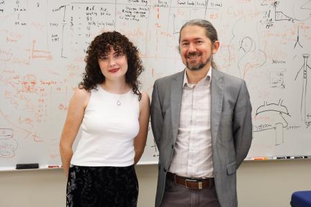 Ph.D. student Anna Neville and Professor Pawel Misztal stand in front of a whiteboard in Misztal's office. 